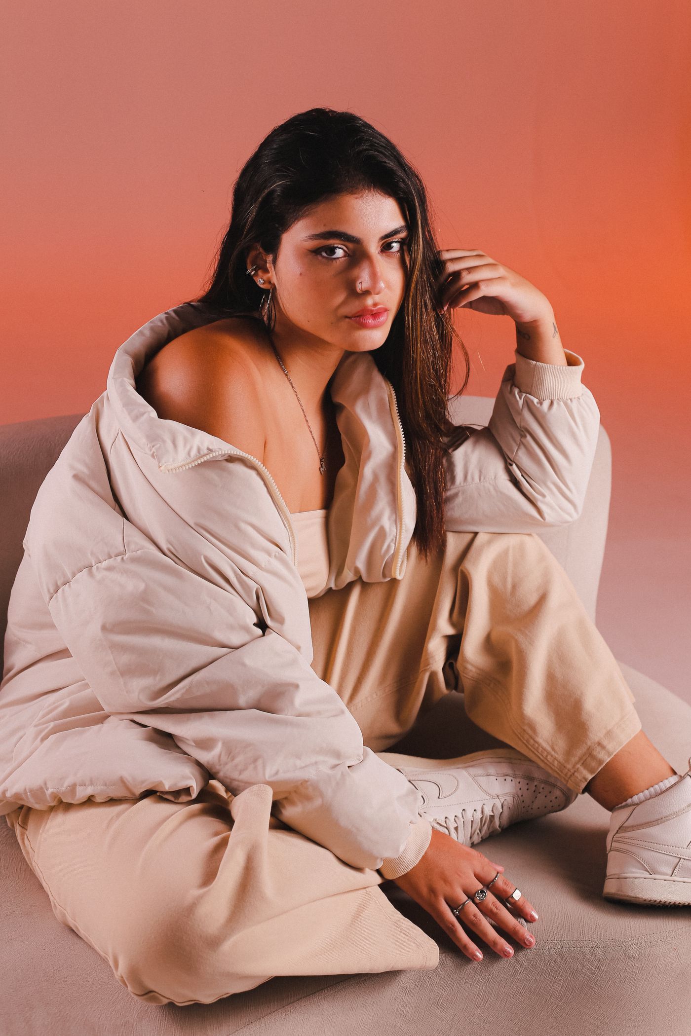 Modelo con chaqueta crema y pantalón beige sobre un fondo terracota